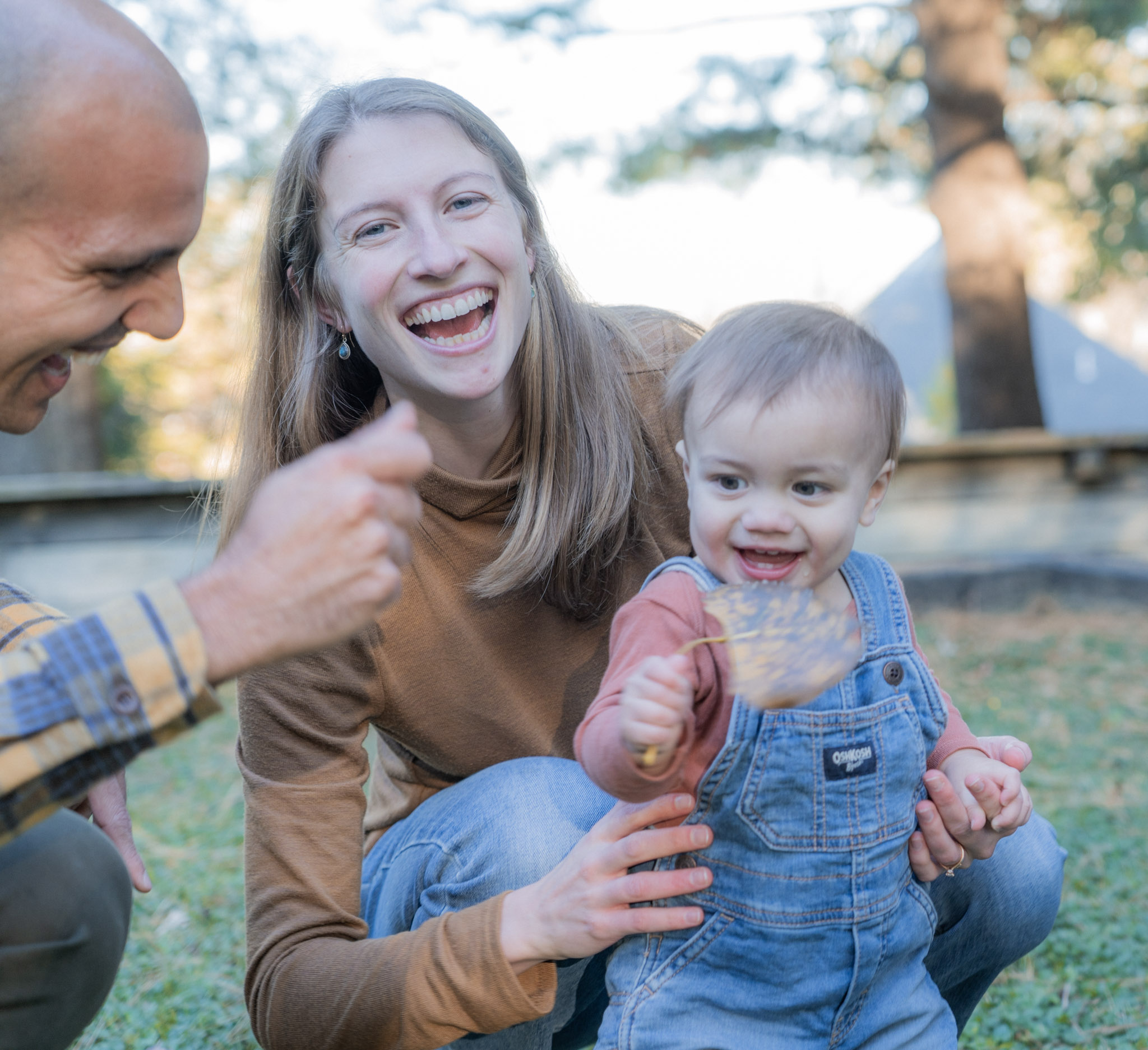 A child holds an autumn leaf close to the camera as the parents laugh